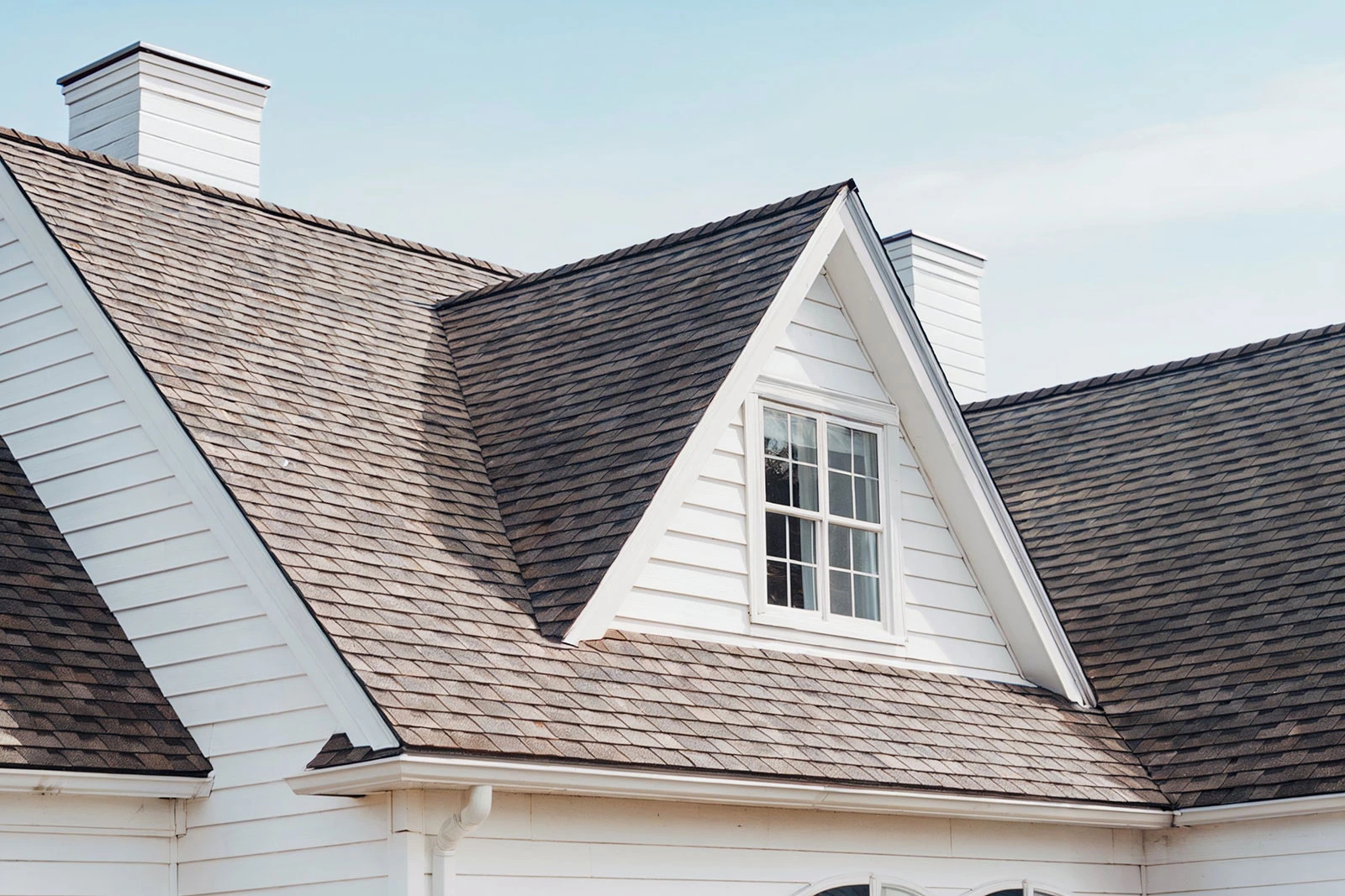 Gabled roof with brown shingles and white siding beneath a clear blue sky.